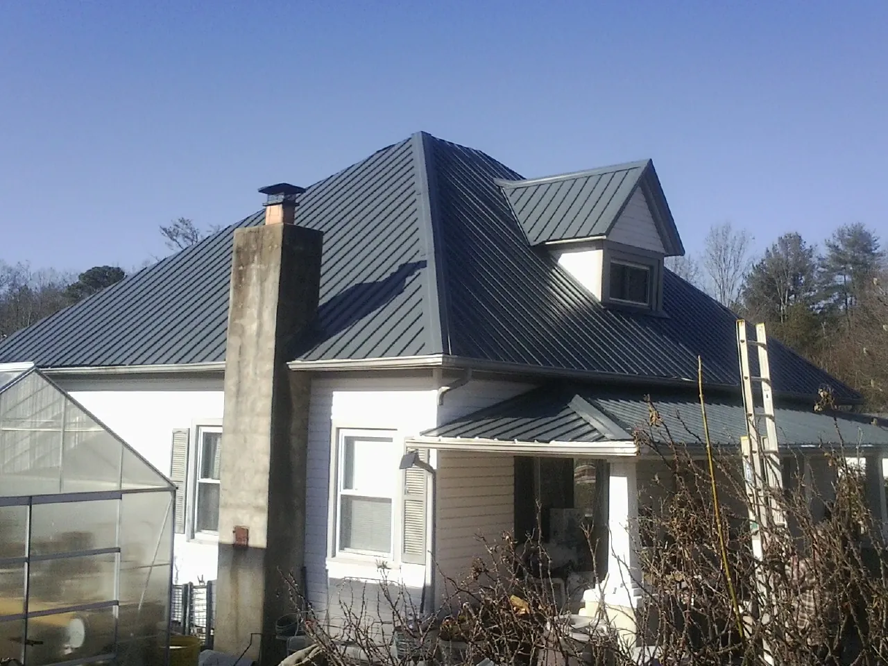 Dark blue standing seam metal roof on a white farmhouse with dormer — Slate & Tile Roof Repair by Roofing Brothers in Starford