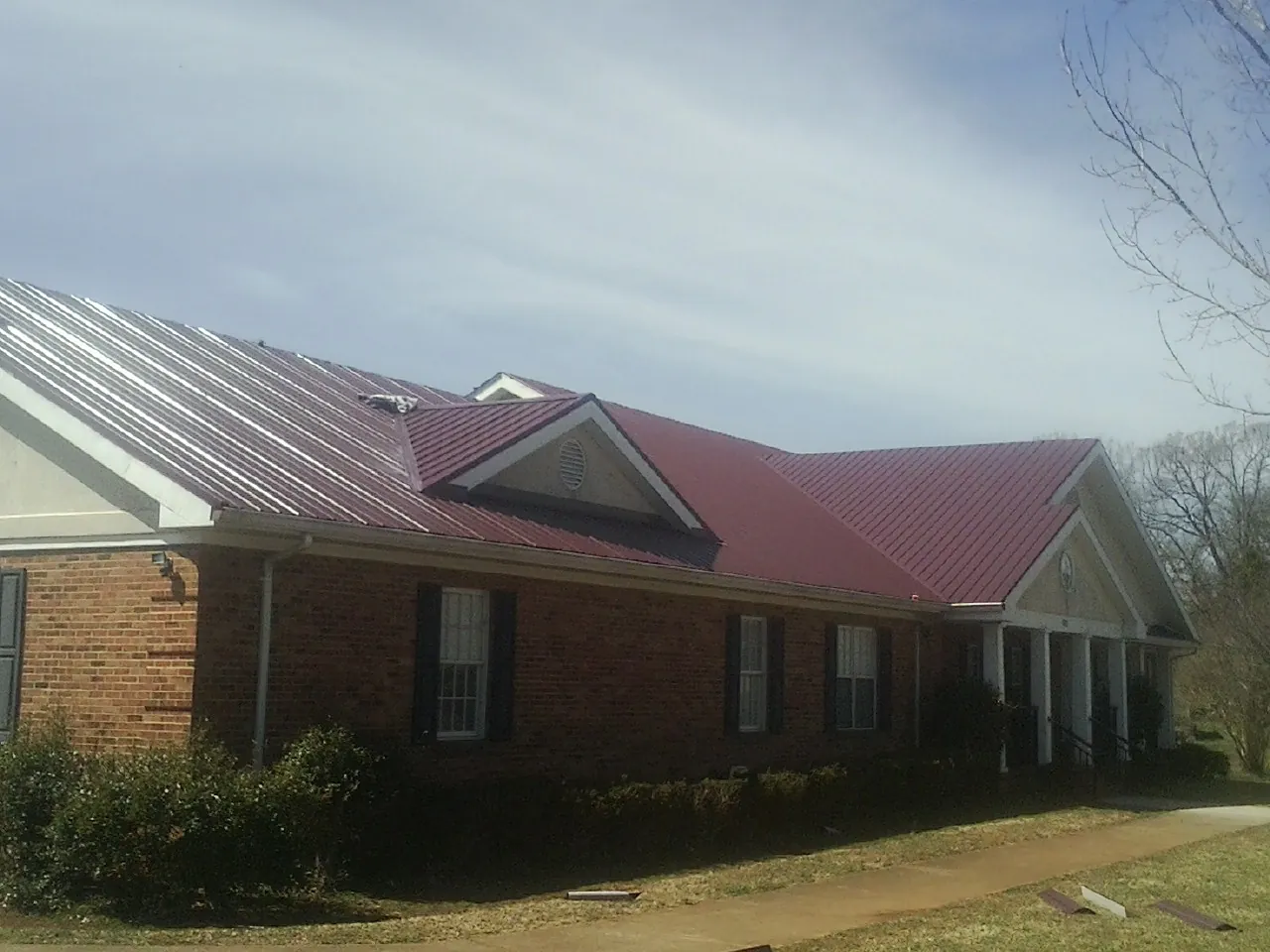 Red metal roof with gabled entries on a long brick building, from a Hail Damage Roof Repair job in Starford