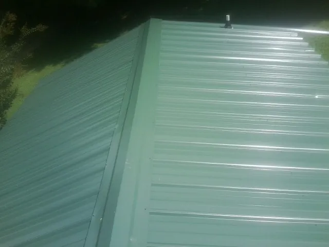 New green metal panels meeting at the ridge of a roof — Flat Roof Repair work by our crew in Starford
