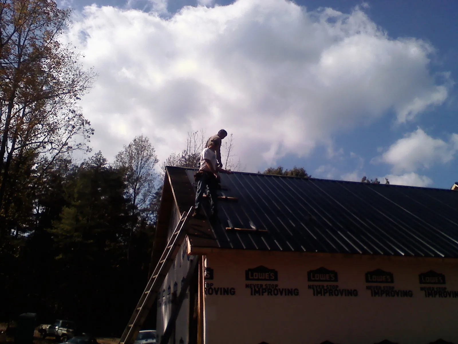 Roofer fastening dark metal panels high against a cloudy sky, from a Roof Inspection job in Starford