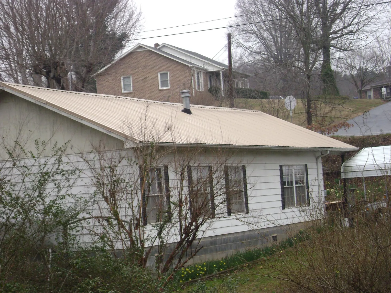 Tan metal roof on a white sided house set into a hillside — Commercial Roofing by Roofing Brothers in Starford